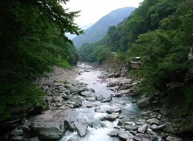 Tree lined river with many rocks and people near the water